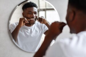 Young man in white t-shirt flossing teeth in front of circular mirror